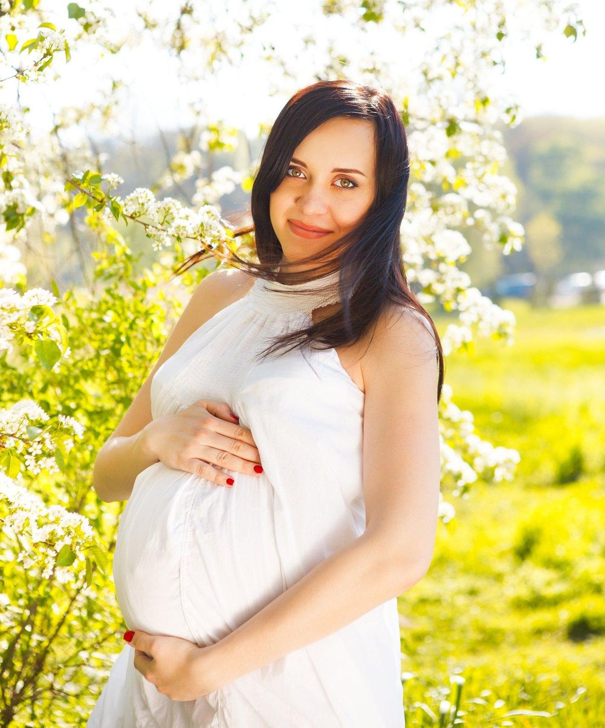Future maman en tenue légère de coton, profitant du printemps en plein air avec un smoothie fruité.