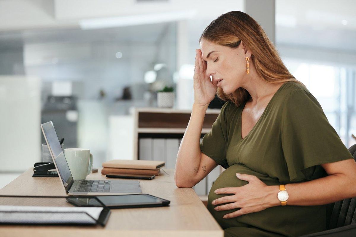Une femme enceinte inquiète, touchant son front, illustrant un mal de tête persistant, signe à surveiller.