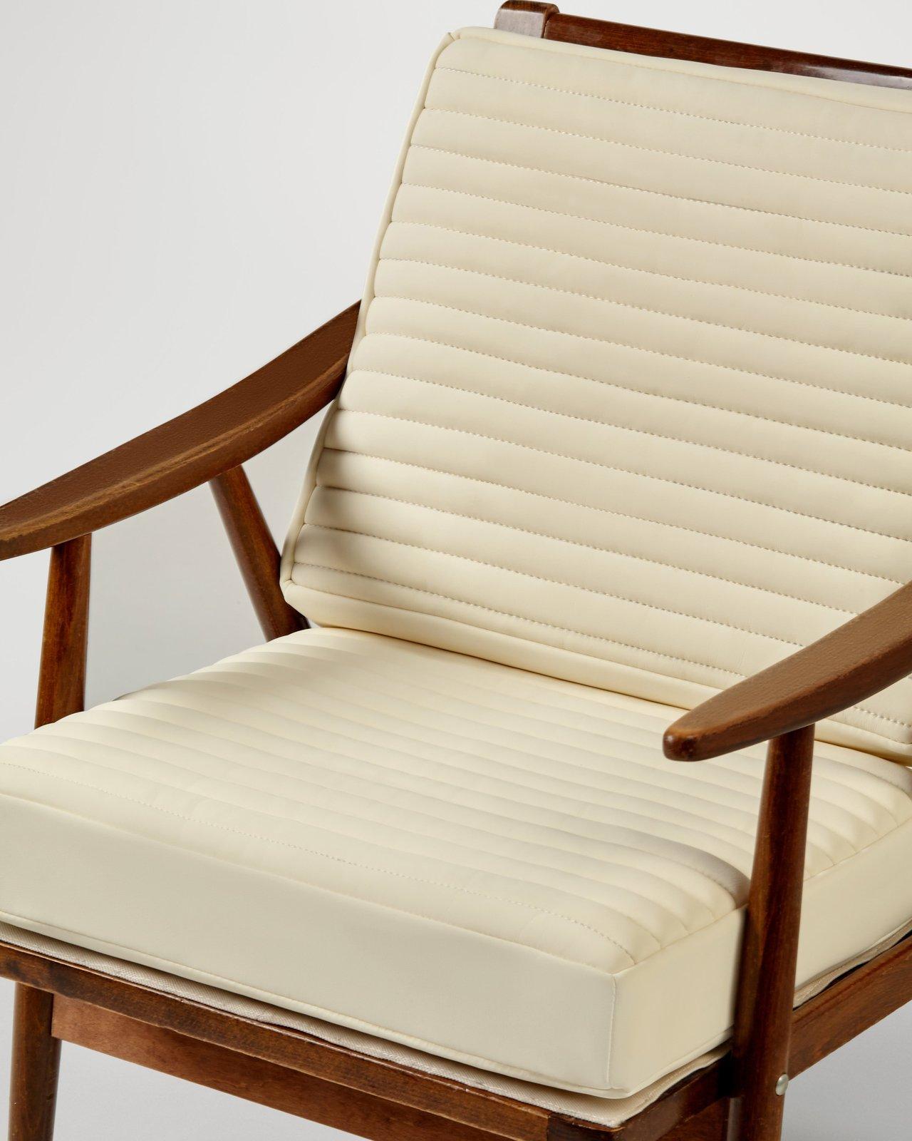 Coin allaitement ergonomique dans un petit appartement, équipé d'un fauteuil en bois, coussin crème et étagères.