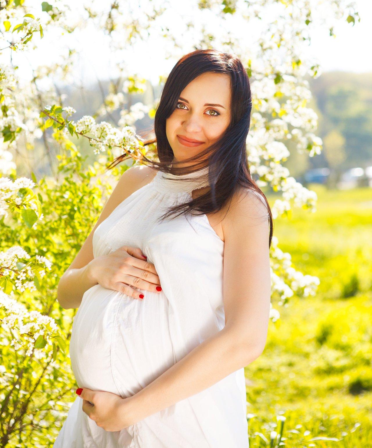 Future maman en tenue légère de coton, profitant du printemps en plein air avec un smoothie fruité.