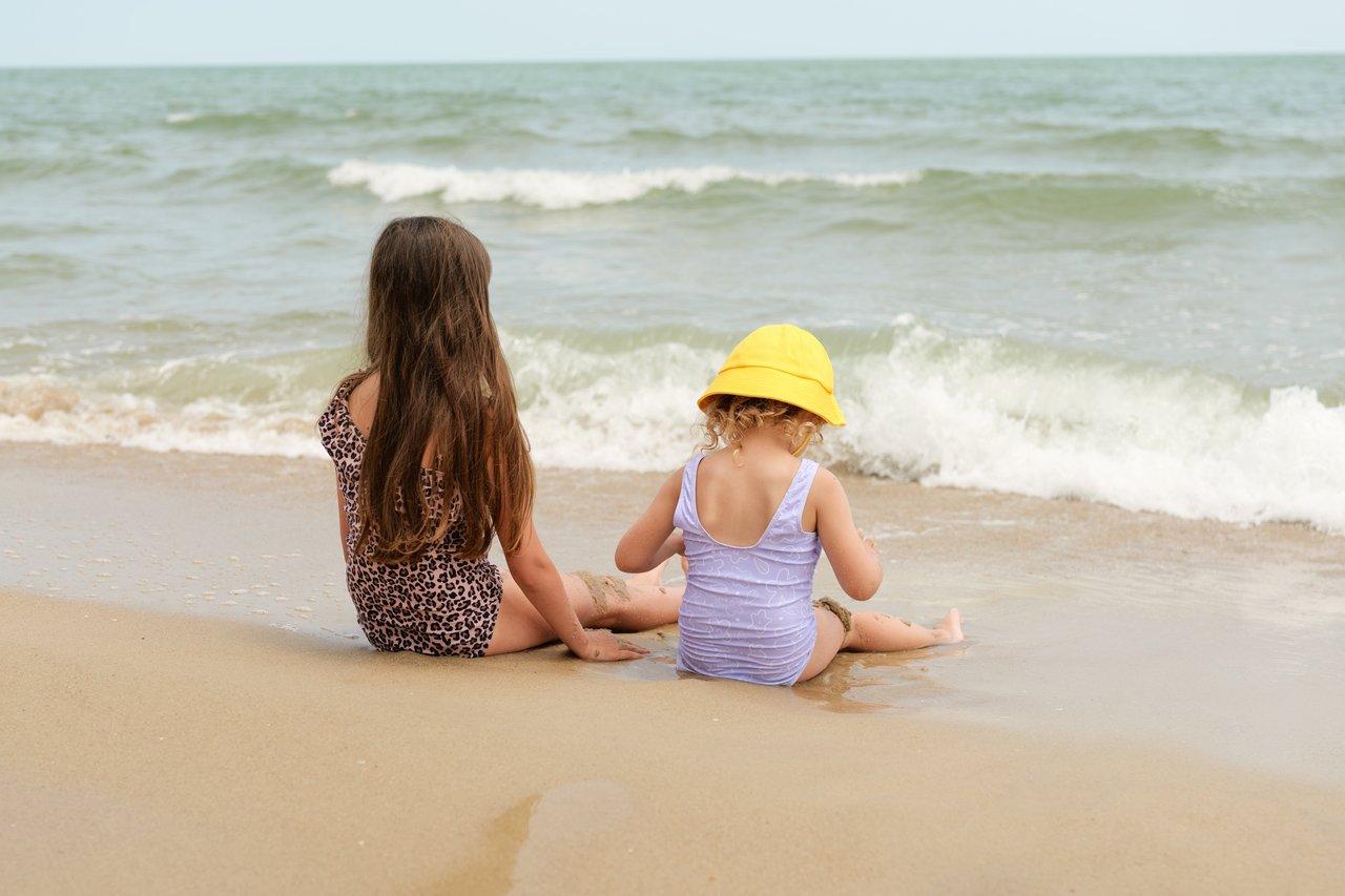 Baby sun protection beach : nourrisson protégé sous tente anti-UV sur plage ombragée avec chapeau et crème solaire.